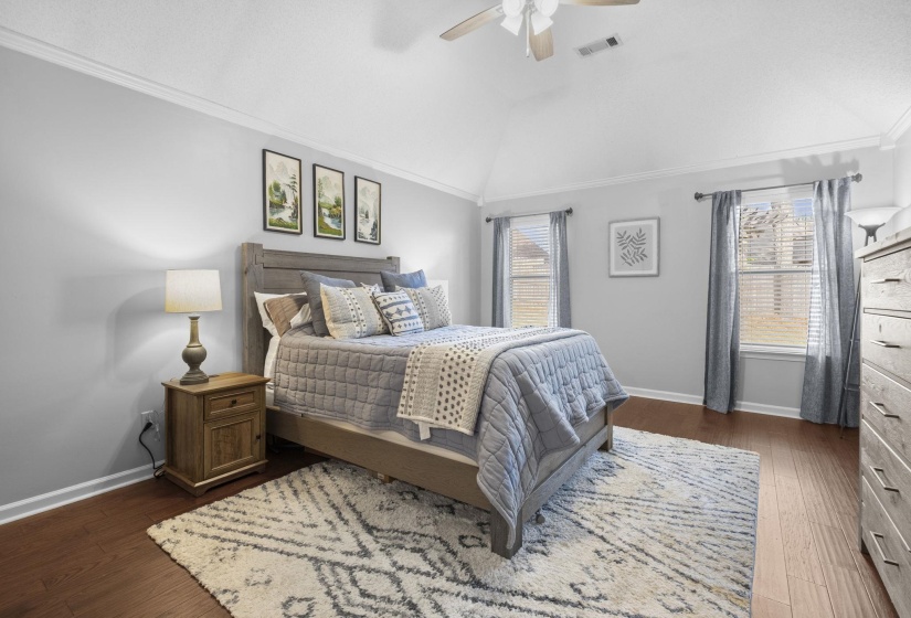 Vaulted ceiling bedroom featuring wood-finish flooring, crown molding, and two windows with blinds