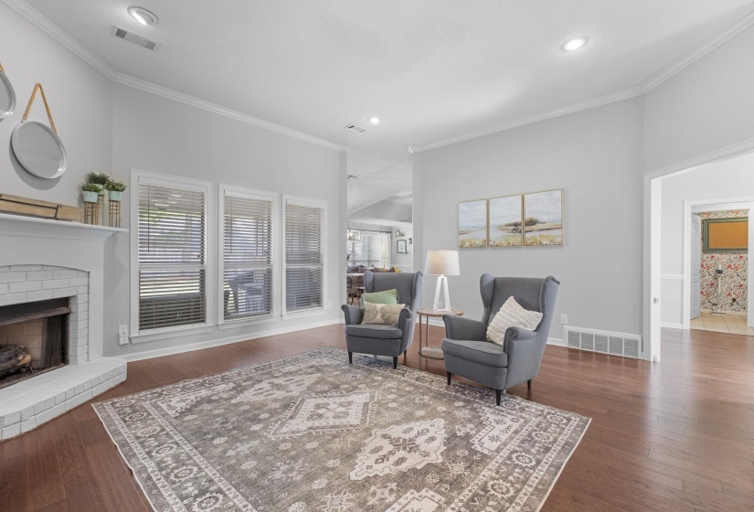 Living area featuring wood-finish flooring, a white brick fireplace, three windows with blinds, and recessed lighting