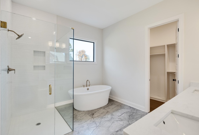 Full bath with a stall shower, a freestanding tub, double vanity, a spacious closet, and light marble finish floors