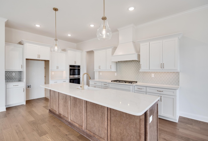 Dual tone kitchen with a kitchen island with sink, dual tone cabinetry, light wood-type flooring, backsplash, and stainless steel appliances