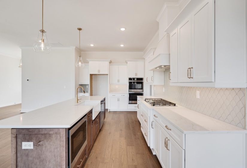 Kitchen with an island with sink, light wood-type flooring, stainless steel appliances, ornamental molding, and light stone counters