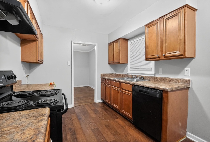 Kitchen with black appliances, exhaust hood, brown cabinetry, dark wood finished floors, and light countertops