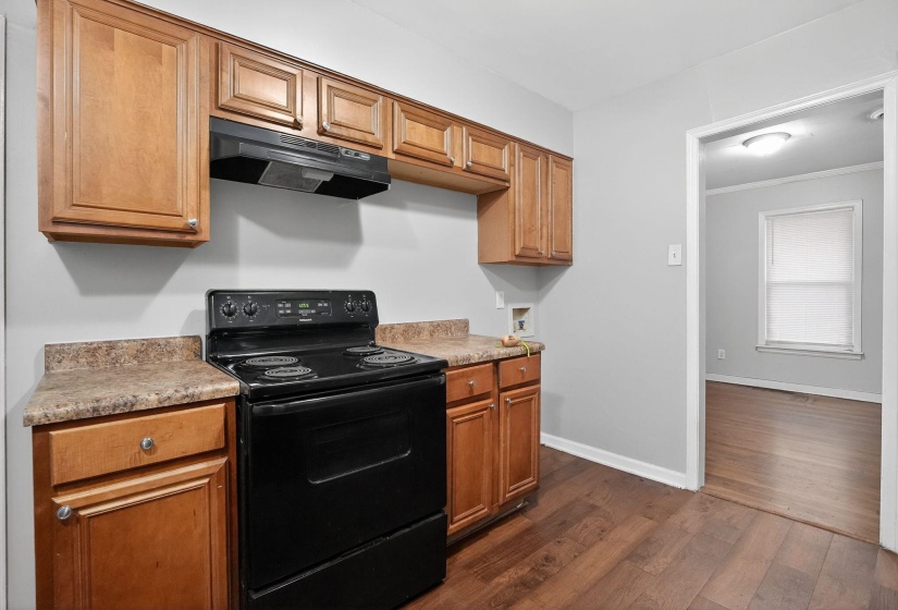 Kitchen featuring black electric range, under cabinet range hood, dark wood-type flooring, brown cabinetry, and light countertops
