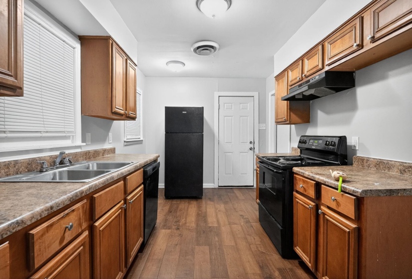 Kitchen featuring black appliances, dark wood-style floors, brown cabinets, under cabinet range hood, and dark countertops