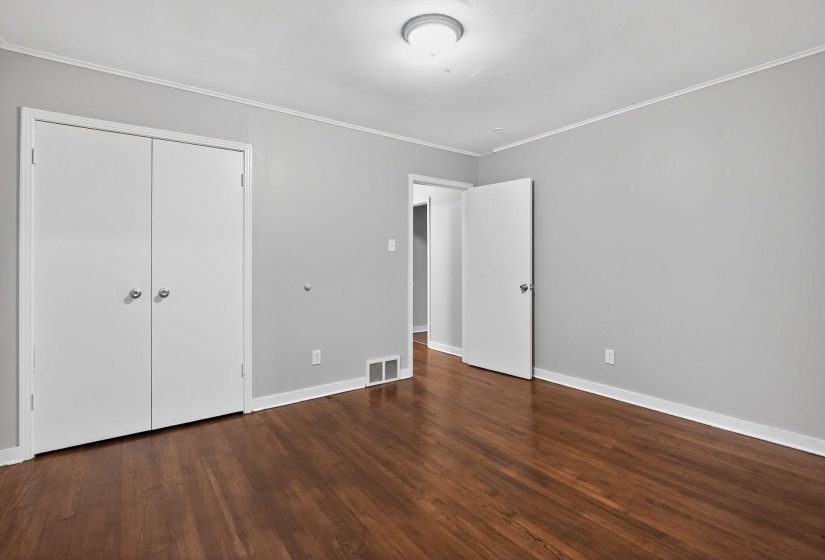 Unfurnished bedroom featuring dark wood-style floors, ornamental molding, and a closet