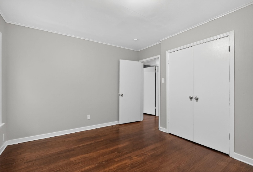 Unfurnished bedroom featuring dark wood-style flooring, crown molding, and a closet