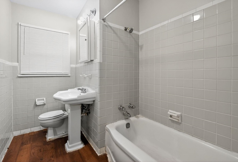 Bathroom with bathtub / shower combination, dark wood-style floors, tile walls, and a wainscoted wall
