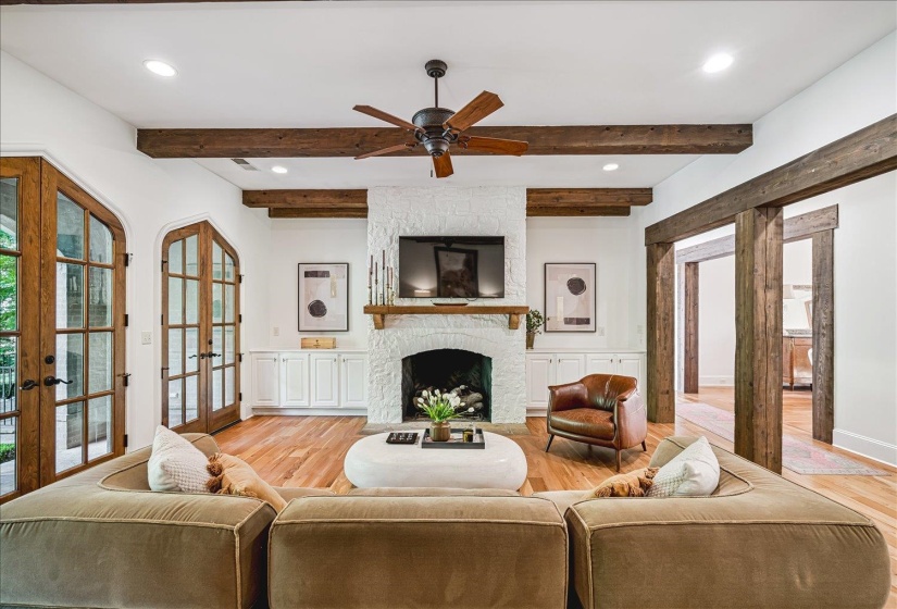 Living area featuring a white-painted brick fireplace, wood-finish flooring, and exposed ceiling beams