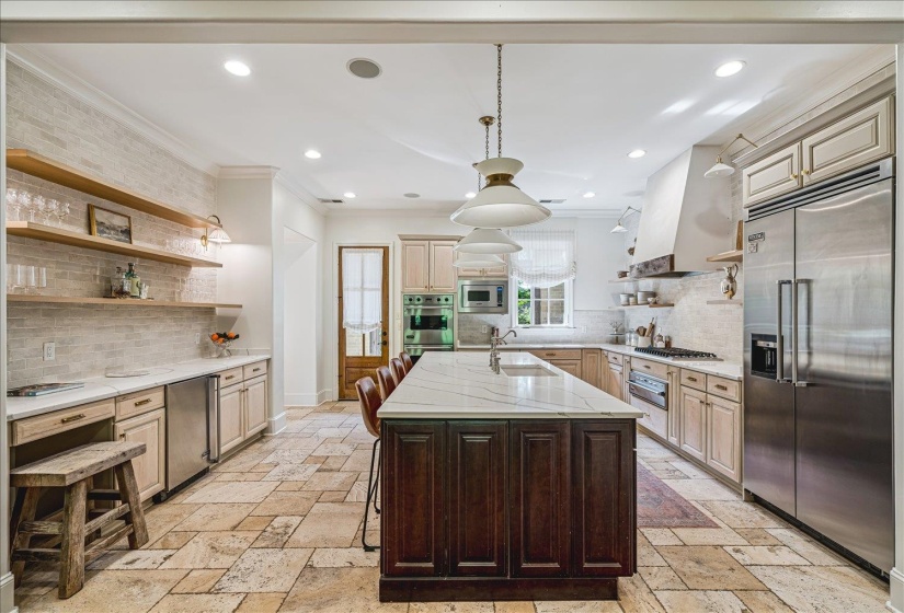 Spacious kitchen featuring a large central island with a white marble-finish countertop, stainless steel appliances, open shelving, tile flooring, and a subway tile backsplash