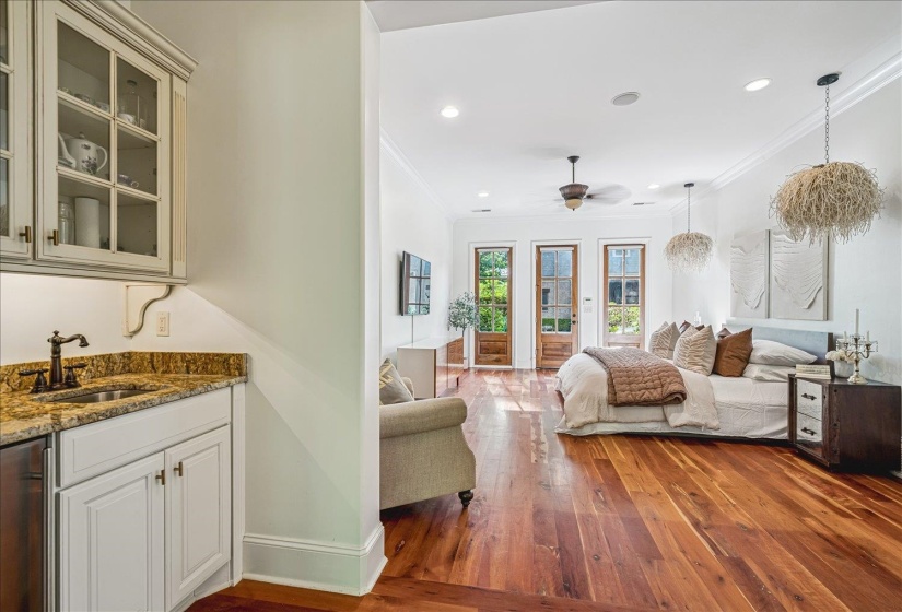 Spacious room featuring wood-finish flooring, a built-in wet bar with a granite countertop and sink, and three paneled glass doors