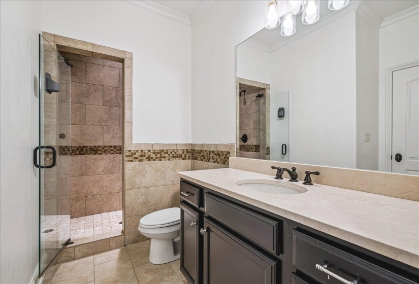 Glass-enclosed shower with tiled walls and floor, vanity with an undermount sink, dark cabinetry, light countertop, and wall-mounted mirror