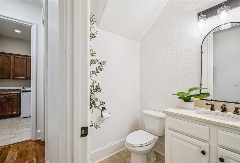Powder room featuring a white single-sink vanity with a light-toned countertop, a black-framed arched mirror, and a two-light fixture