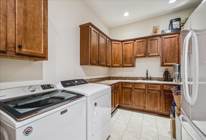 Utility room featuring light wood-finish cabinetry, a built-in sink with a black faucet, light-toned countertops, and light square floor tiling