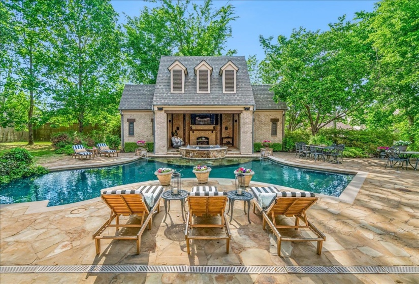 Resort-style backyard featuring a free-form swimming pool with stone coping, extensive flagstone patio, and a dedicated pool house