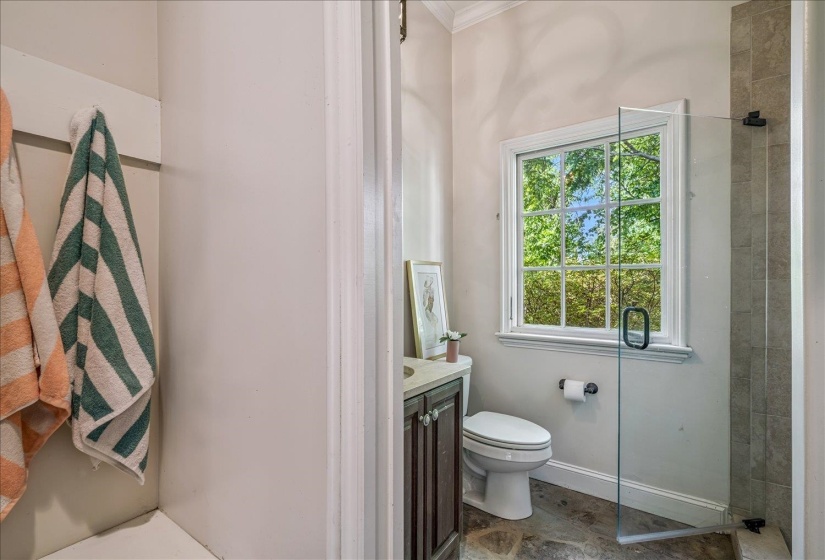Bathroom featuring a framed window, a dark wood-finish vanity with a light-toned countertop, a toilet, and a glass-enclosed shower with tiled walls