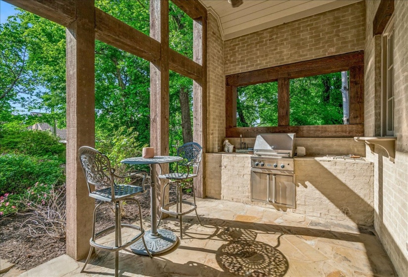 Covered patio featuring an outdoor kitchen with built-in stainless steel grill and sink, flagstone flooring, and exposed wood beam accents
