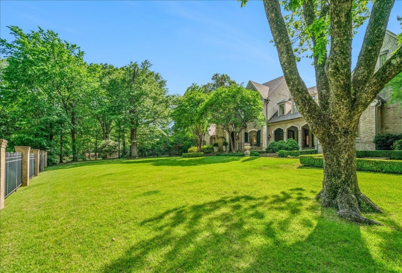 Expansive landscaped lawn with mature trees and a brick and iron fence