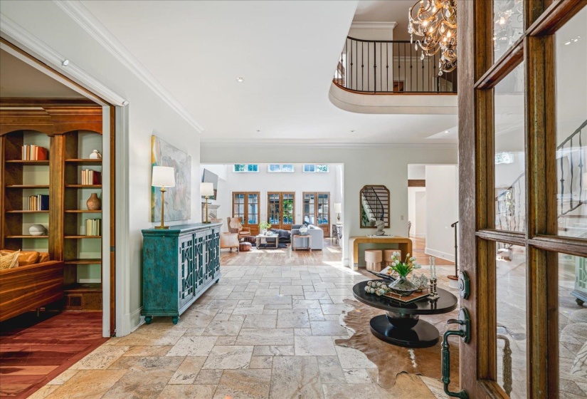 Grand foyer featuring large format stone tile flooring, a curved upper-level balcony with iron railings, and a crystal chandelier
