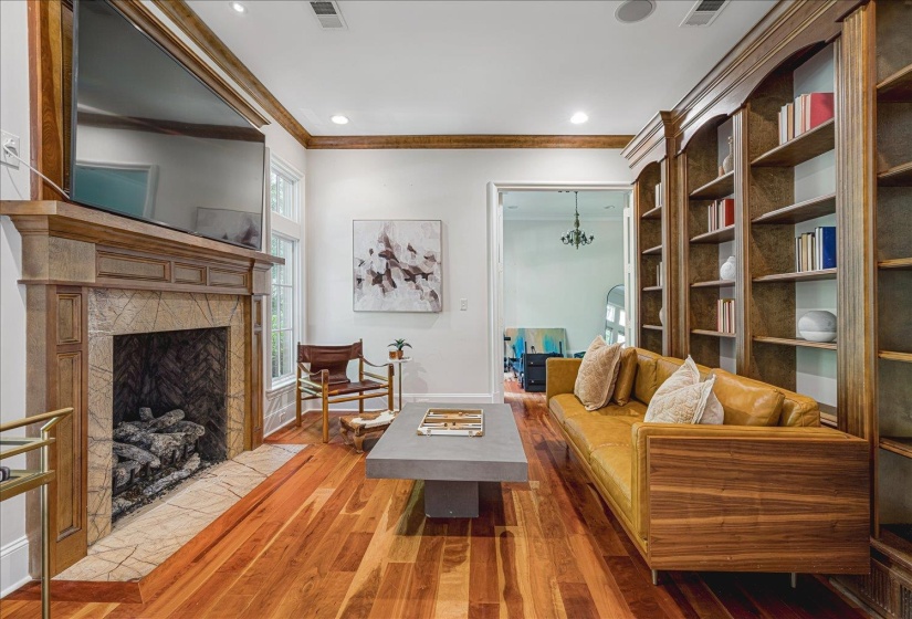 Spacious room featuring rich wood-finish flooring, a stone-surround fireplace with a wood mantle, and built-in wood shelving