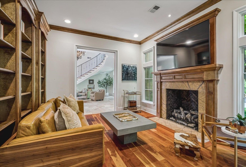 Warm living space featuring rich wood-finish flooring, a built-in fireplace with a stone surround and wood mantle, and an extensive built-in wooden bookcase