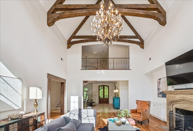 Vaulted ceiling with exposed wood beams, an ornate chandelier, and a second-story interior balcony with wrought iron railing