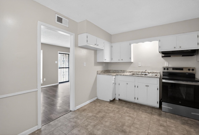 Kitchen with electric stove, light countertops, white cabinets, and light tile patterned flooring