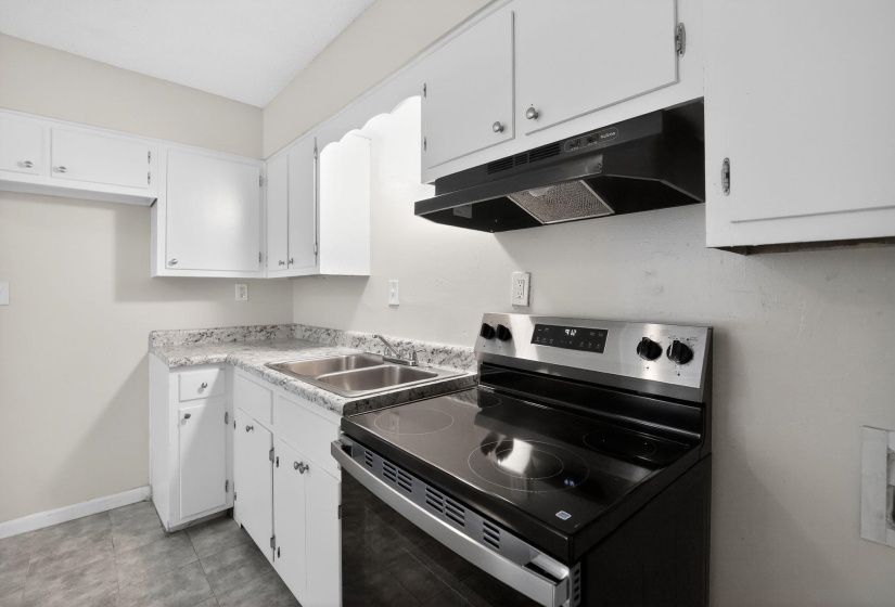 Kitchen with stainless steel range with electric cooktop, white cabinetry, and light countertops
