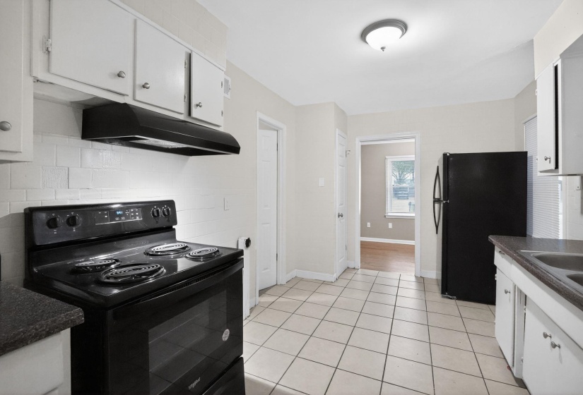 Kitchen with black appliances, white cabinets, light tile patterned flooring, and tasteful backsplash