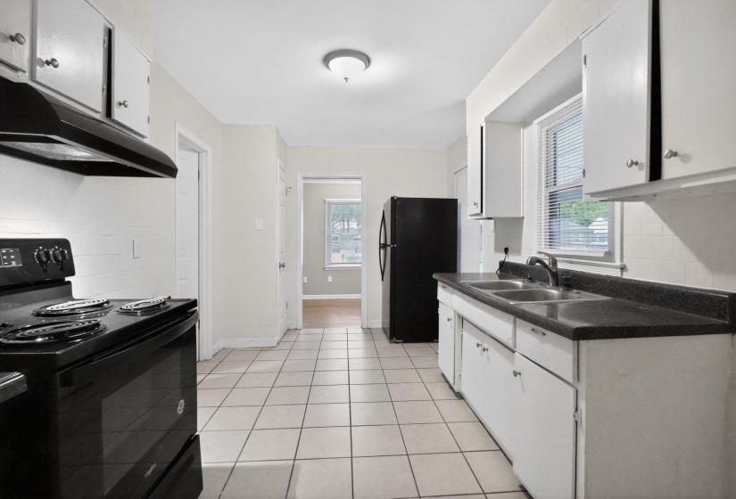 Kitchen featuring black appliances, backsplash, white cabinets, dark countertops, and light tile patterned flooring