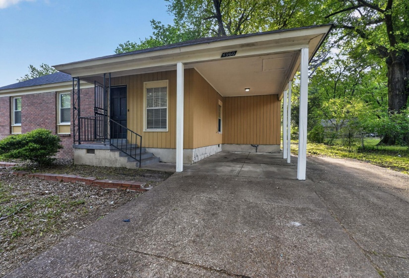 Brick and siding exterior featuring a covered carport, concrete driveway, and a front porch with wrought iron railings