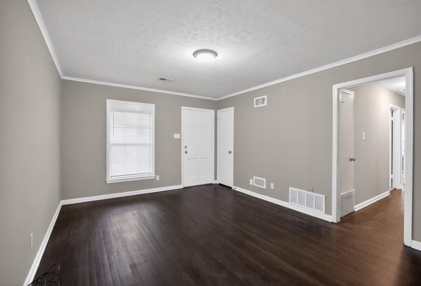 Spacious room featuring dark wood-finish flooring, light neutral-toned walls, and bright white trim
