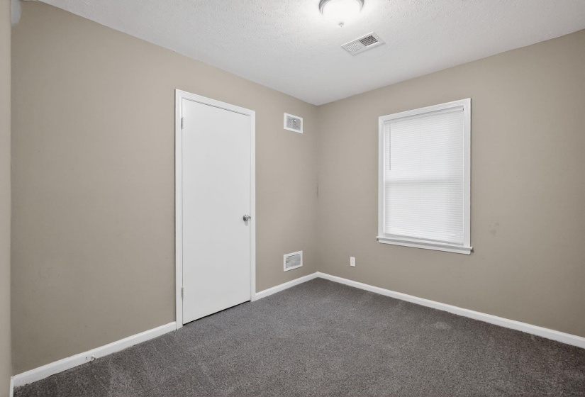 Interior room featuring neutral wall paint, dark gray carpeting, a single window with blinds, a white interior door, and a flush mount ceiling light