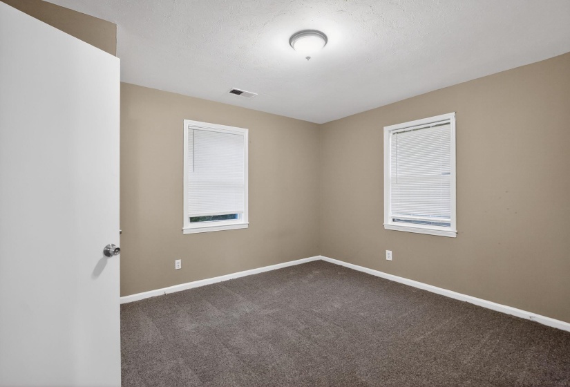 Neutral-toned room featuring two windows with white blinds, wall-to-wall carpeting, and a flush-mount ceiling light fixture