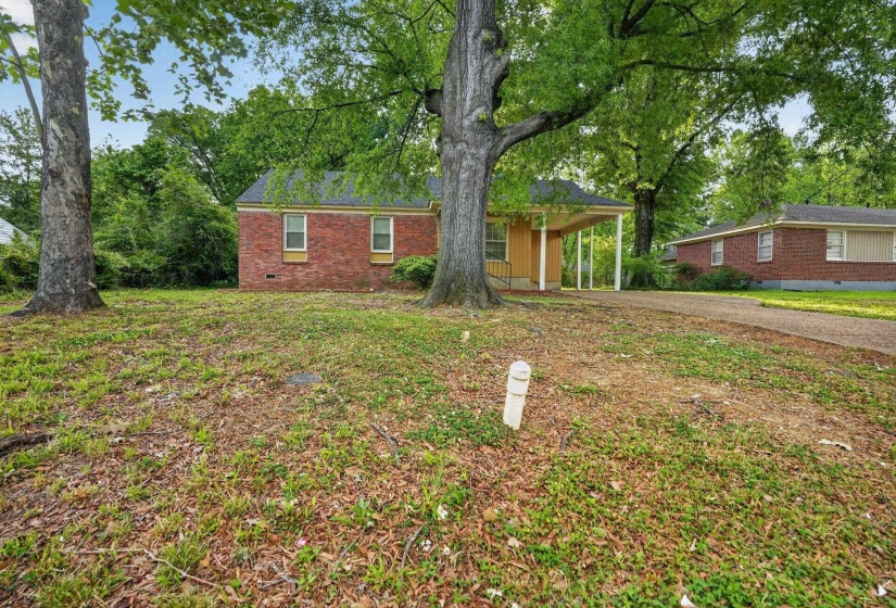 Brick facade residence with a covered carport, mature trees, and an extended driveway