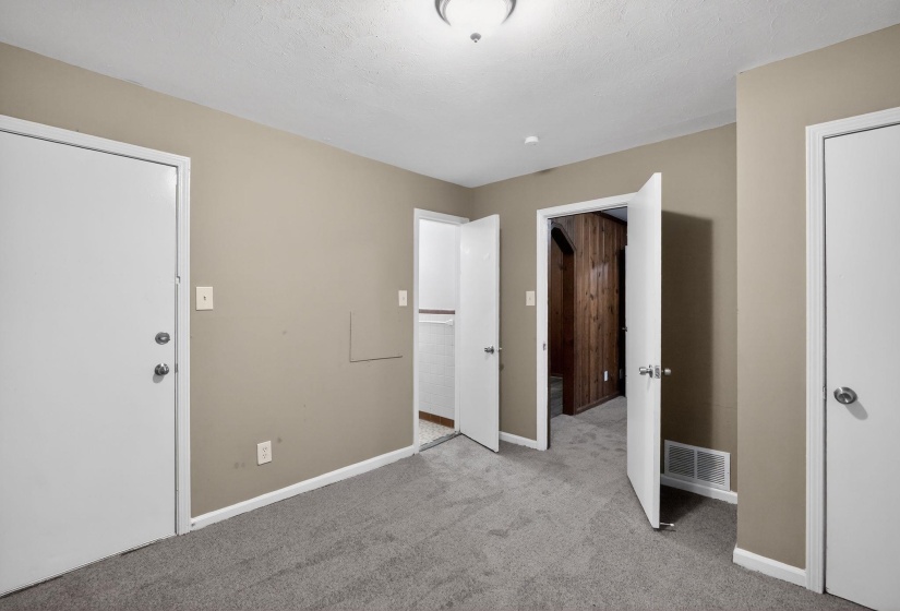 Carpeted room featuring neutral-toned walls, white trim, and multiple white doors with round silver hardware