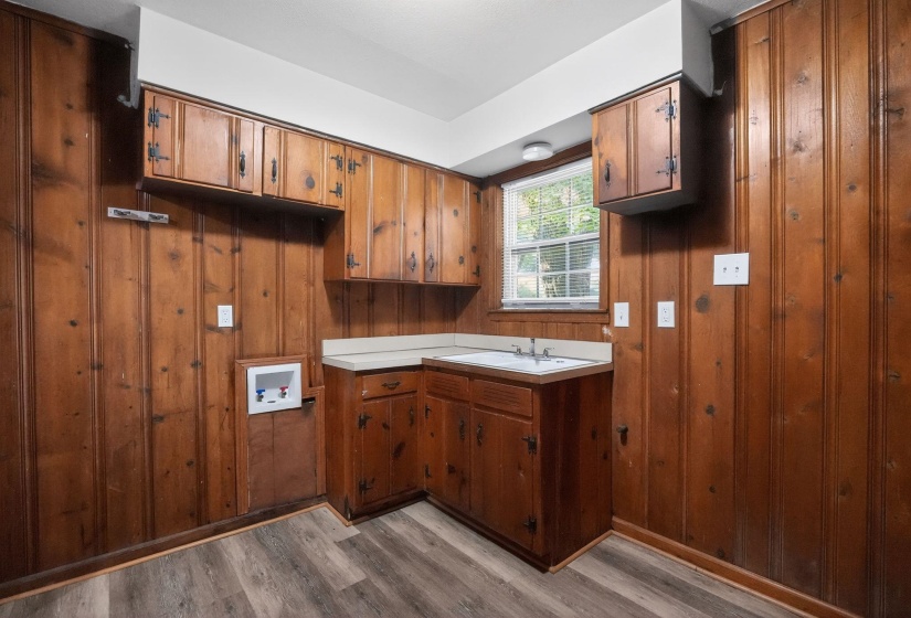 Utility room featuring wood paneling, wood-finish flooring, a built-in utility sink, and ample cabinetry