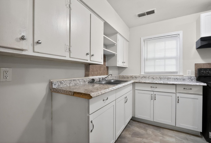 Kitchen featuring white cabinetry, a double basin stainless steel sink, tiled backsplash, and a black range