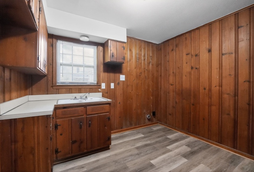 Utility room featuring wood-paneled walls, a single-basin sink with a white countertop, and wood-finish flooring