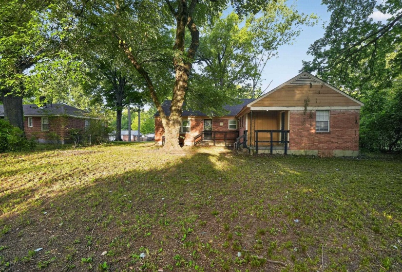 Expansive rear yard featuring mature trees and a brick-clad home with a gabled roofline