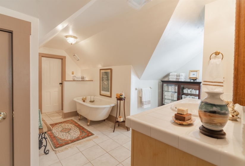 Bathroom with vaulted ceiling, tile patterned flooring, and a bathtub. Attic access through door