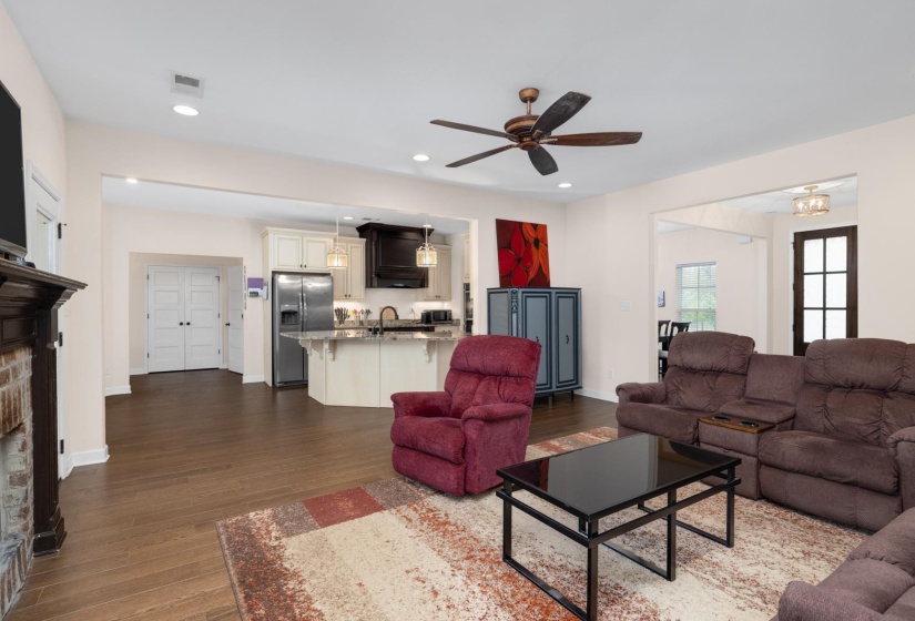 Spacious living area featuring wood-finish flooring, a brick fireplace with a dark wood mantel, and a ceiling fan with integrated lighting