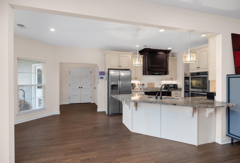 Open-concept kitchen and living area featuring dark wood-finish flooring, a kitchen island with stone countertops, stainless steel appliances, white cabinetry, and recessed lighting