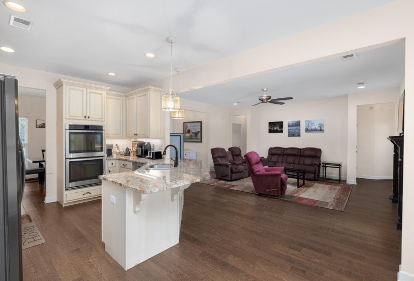 Open concept kitchen featuring an island with a stone countertop, pendant lighting, stainless steel double ovens, and wood-finish flooring