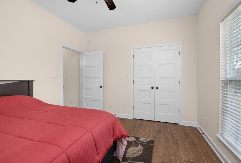 Bedroom featuring wood-finish flooring, white panel doors, and a window with blinds