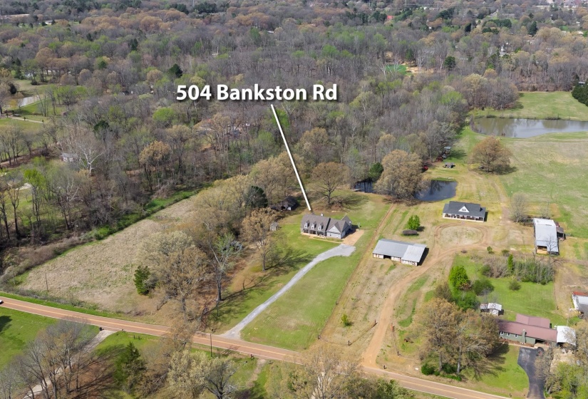 Expansive property featuring a central residence, multiple accessory structures, two visible ponds, and a gravel driveway