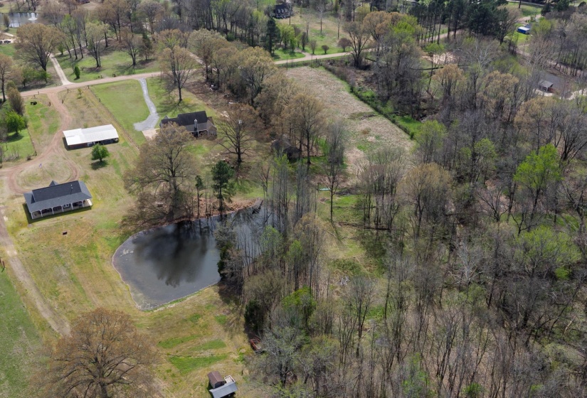 Expansive property featuring a private pond, two residential structures, a large outbuilding, and mature trees throughout