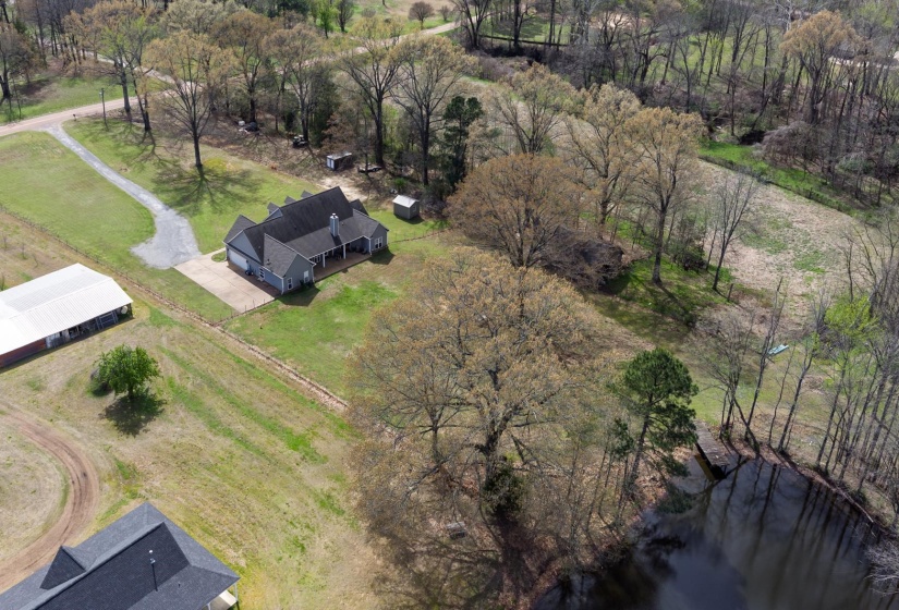 Spacious property featuring a single-story residence with an attached garage, a large detached outbuilding, and a pond with a pier