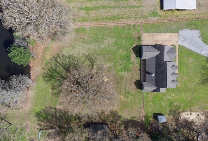 Expansive property featuring a private pond with a wooden dock, mature trees, a main residence with a multi-gabled roof, a paved driveway, and a detached shed