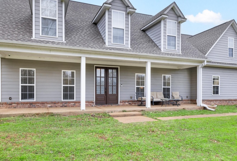 Exterior facade featuring light gray siding, white trim, a covered porch, dark double entry doors with decorative glass, and multiple gabled dormers