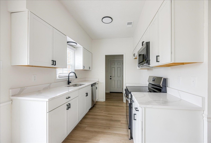 Galley kitchen featuring white cabinetry, light-toned countertops with a subtle vein pattern, and wood-finish flooring